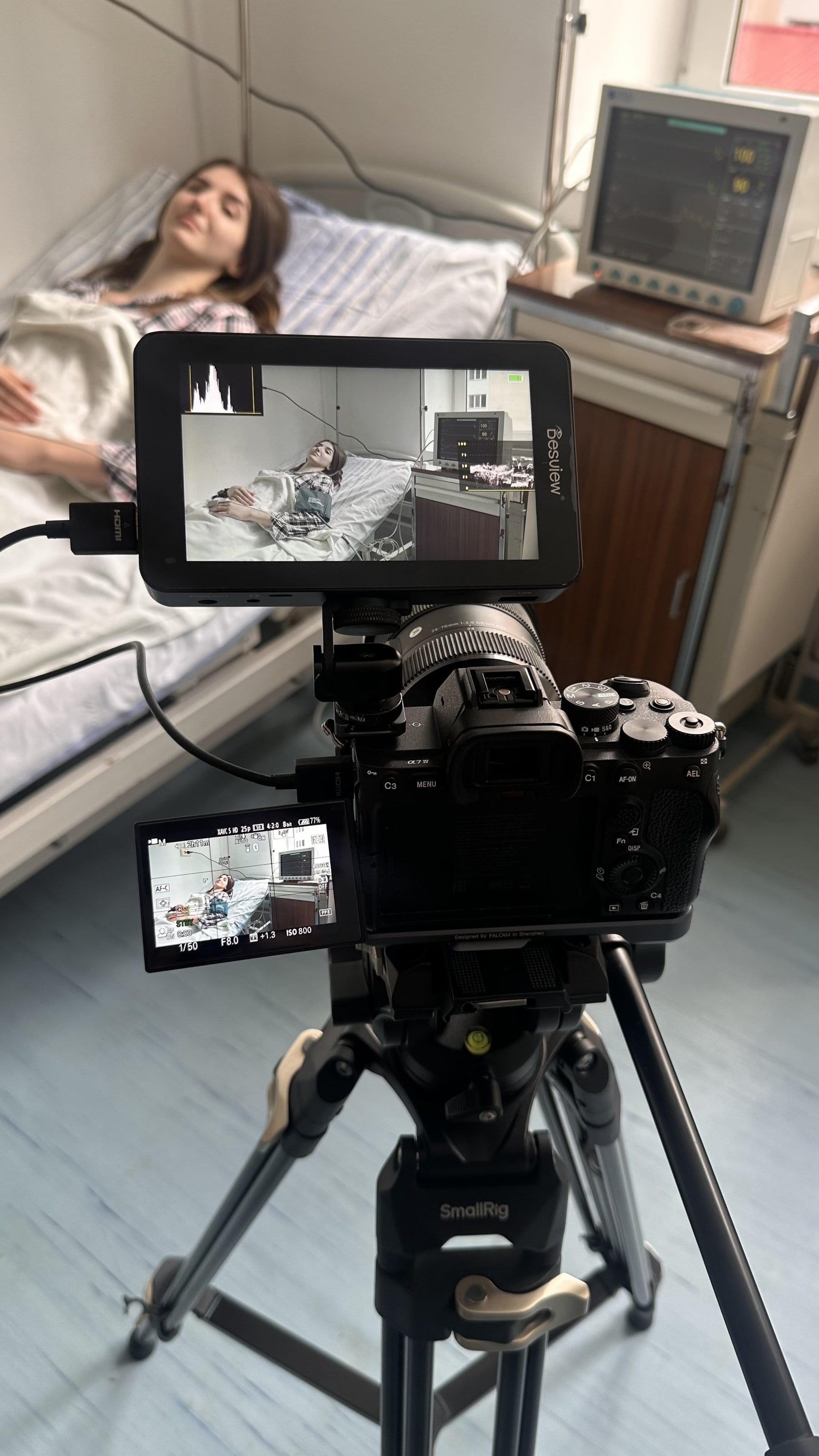 Cameră video pe trepied cu monitor extern, filmând o actriță într-un pat de spital, într-o scenă medicală.