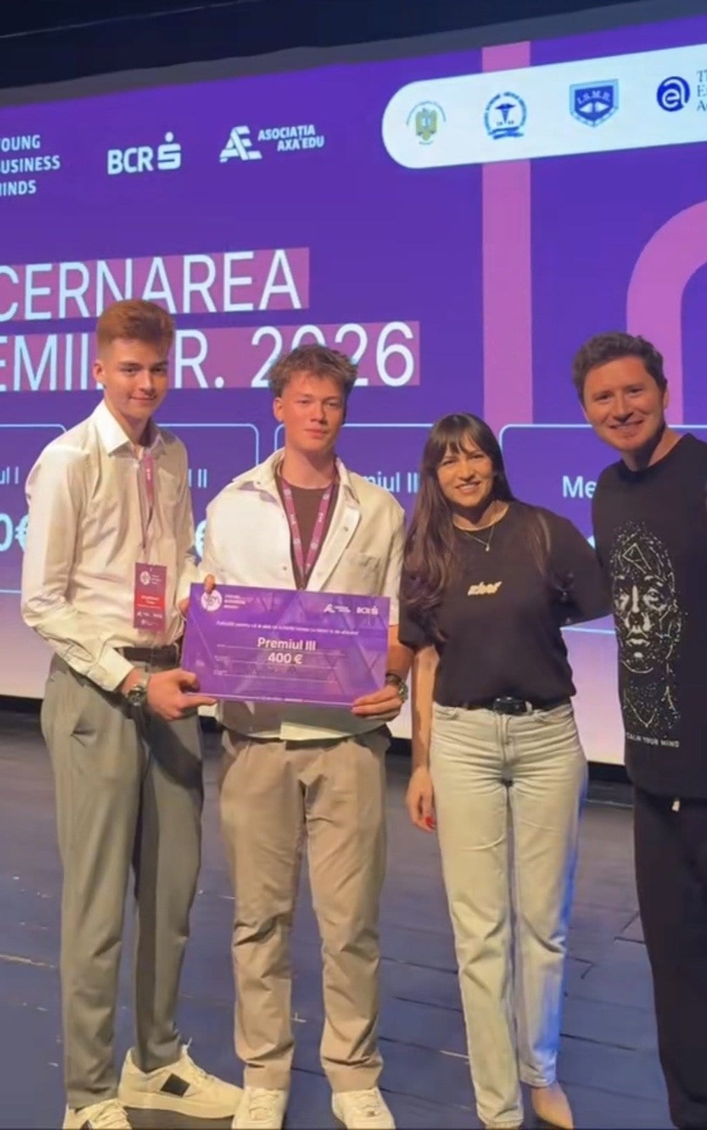 Alexandru Moise pe scenă, alături de un coleg și doi reprezentanți ai juriului, ținând diploma pentru Premiul III la Young Business Minds 2026.